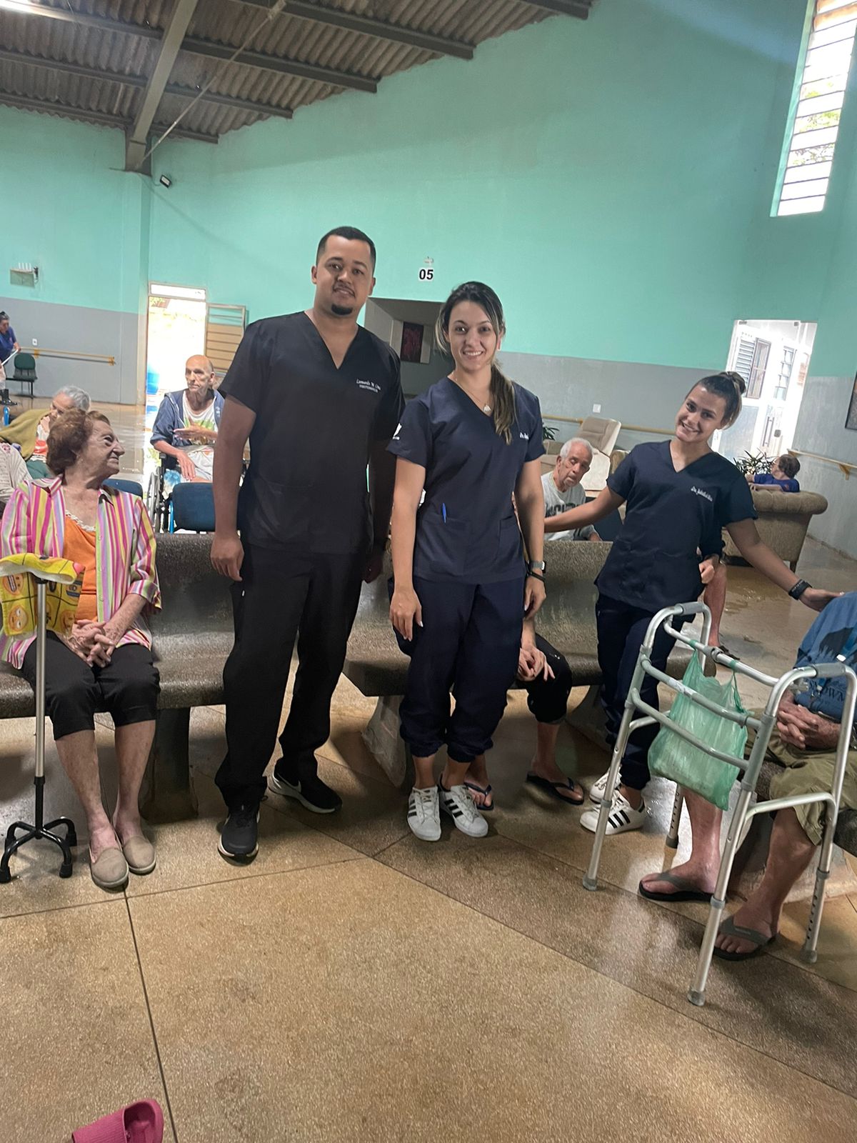 Equipe de enfermagem e apoio, de uniforme azul-marinho, no salão com os residentes