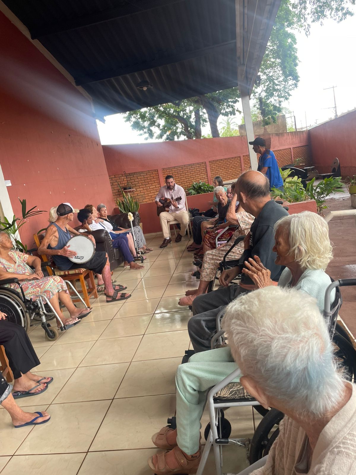 Roda de música na área externa coberta, com violão e residentes acompanhando no pandeiro