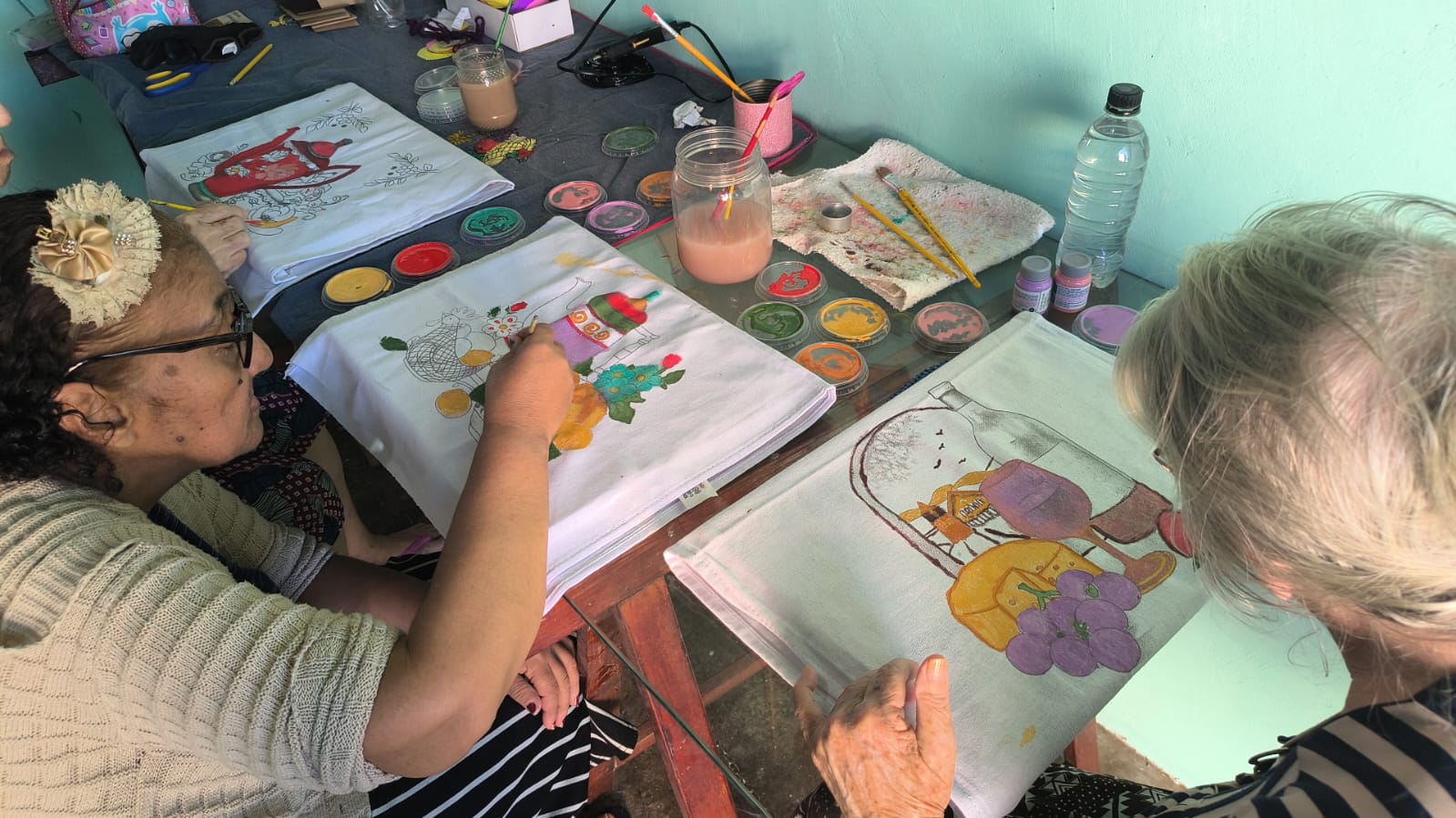 Residentes pintando panos de prato com tintas coloridas em uma oficina de pintura